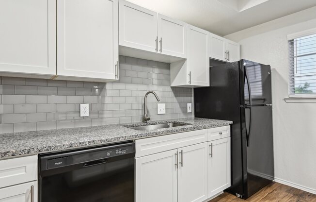 A kitchen with white cabinets and a black refrigerator.