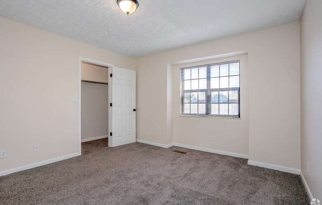 A room with a carpeted floor, a window with blinds, and a door.