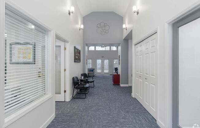 A hallway with a carpeted floor, white walls, and a row of chairs.