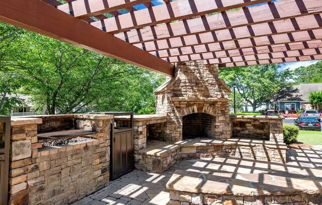 a stone outdoor fireplace with a pergola on top of it