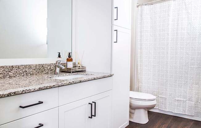 Inviting spare bathroom with elegant granite countertops, resilient stain-resistant plank flooring, and a modern shower.