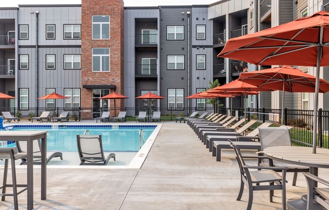 a swimming pool with chairs and umbrellas in front of an apartment building