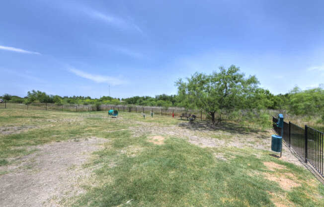 A fenced yard with a tree and a trash can.