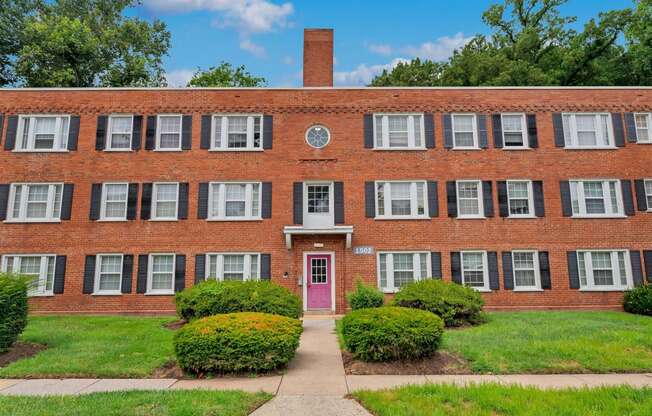 a red brick building with a pink door and grass and bushes