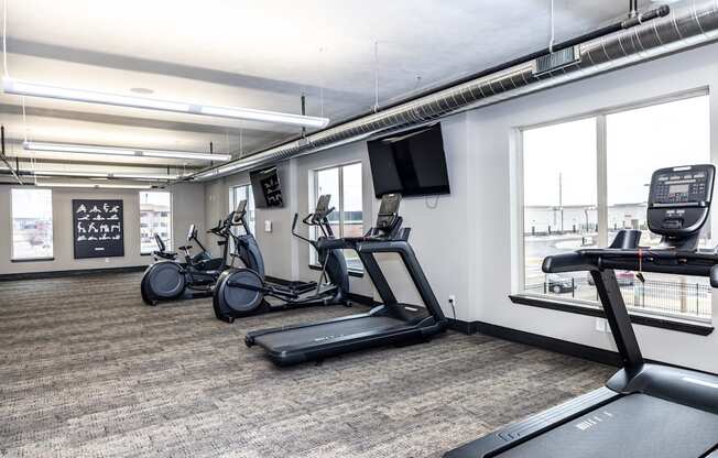 A gym with treadmills, exercise bikes, and a television.