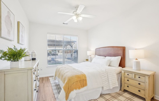 A bedroom with a bed, nightstand, and a plant on the windowsill.