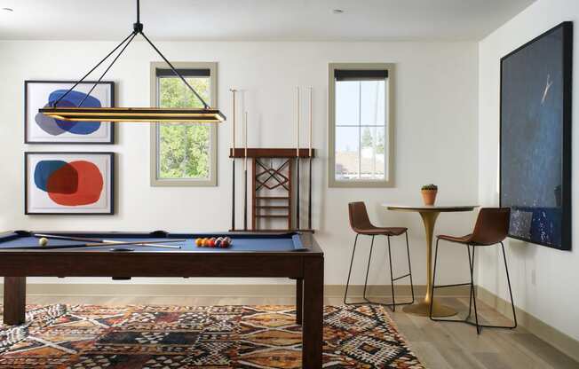 Riverside, CA Luxury Apartments - Lincoln Village - Game Room with Pool Table, Hanging Light, Hhigh-Top Table and Seats, Windows, and Mounted Wall Art