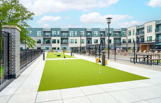 A courtyard with a putting green turf with multiple pins to practice your short game on.