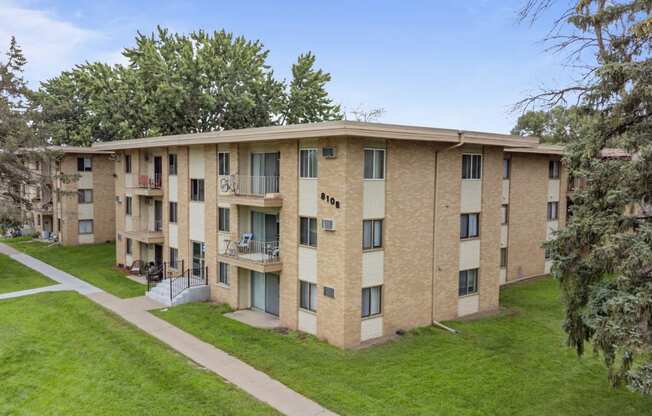 a brick apartment building with a green lawn and trees