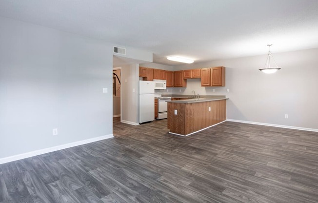 an empty living room and kitchen with wood flooring and white walls