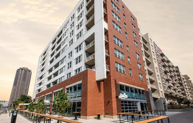 A modern multi-story building with a red brick facade and a balcony with a wooden railing.