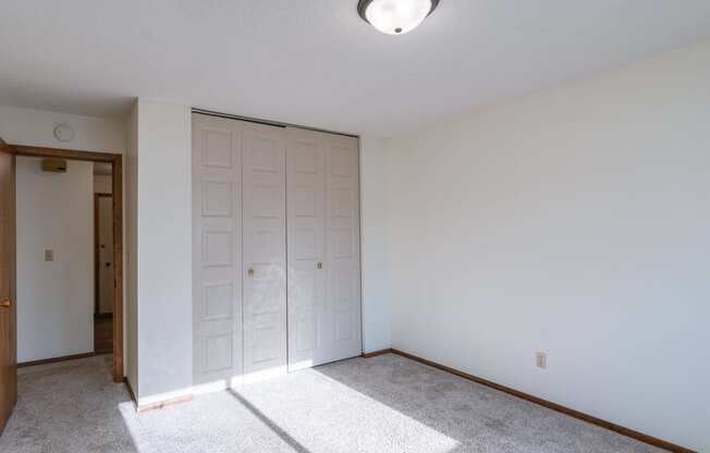 a bedroom with white walls and a door to a closet. Fargo, ND Windsor Apartments