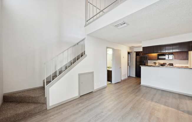 the living room and kitchen of an apartment with white walls and wood floors