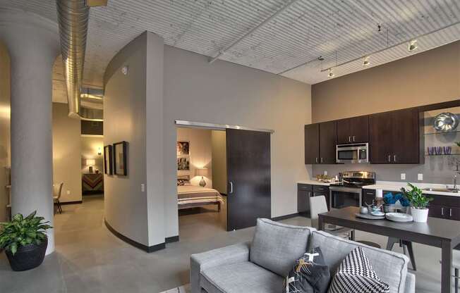 A modern living room with a grey couch and a kitchen area in the background.