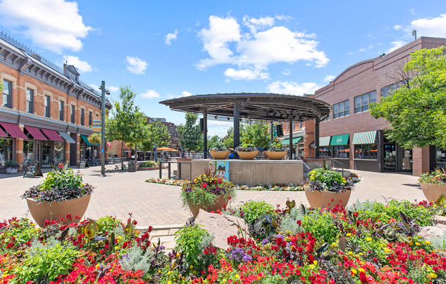 A sunny day in a town square with a gazebo and flower beds.