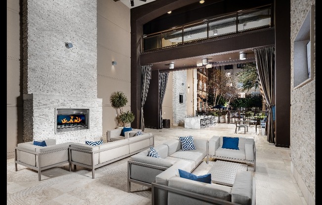 An open-air loggia with a stone fireplace, two seating areas with upholstered couches and armchairs, a dining table, and several patio tables and chairs.