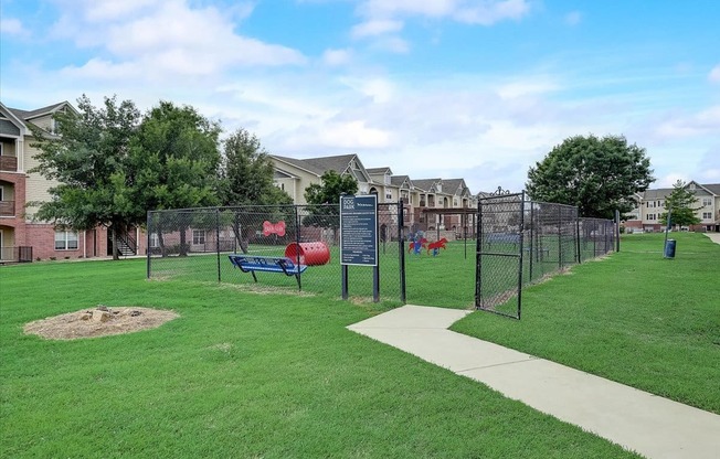 a fenced in park with a playground and houses in the background