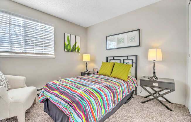 A bedroom with a colorful bedspread and a white chair.