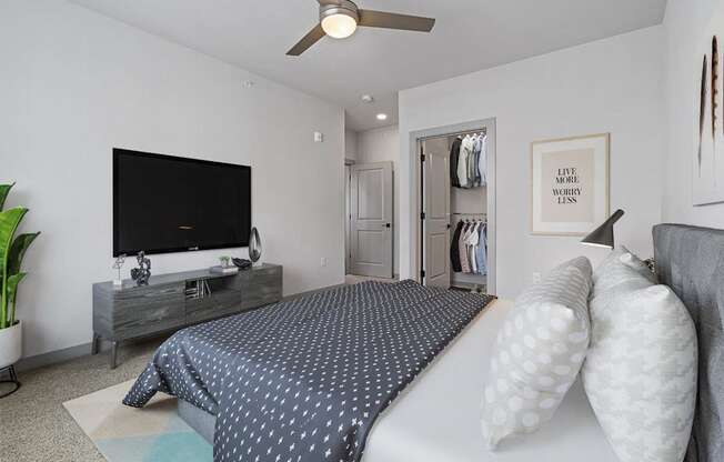 A bedroom with a bed, a television, and a ceiling fan.