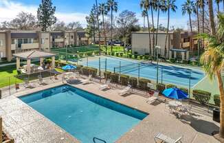 A pool surrounded by palm trees and a tennis court.