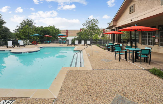 a swimming pool with tables and umbrellas outside of a building