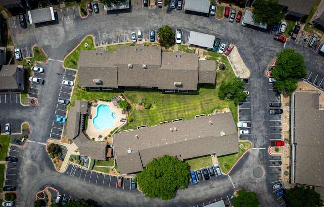 A bird's eye view of a residential area with houses, cars, and a swimming pool.