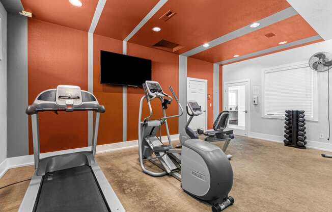 a gym with treadmills and weights and a tv