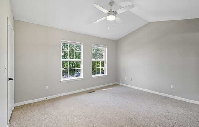 A room with a ceiling fan and two windows.