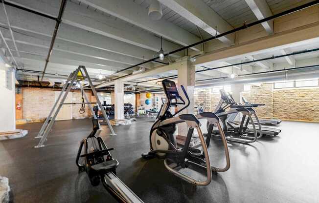 A gym with a row of treadmilers and elliptical machines.
