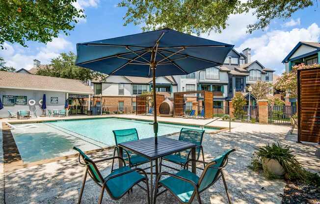 A poolside table with chairs and an umbrella over it.