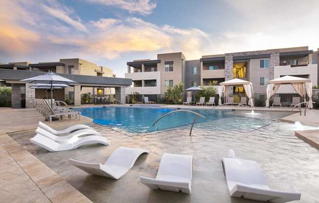 a swimming pool with lounge chairs and umbrellas in front of a building