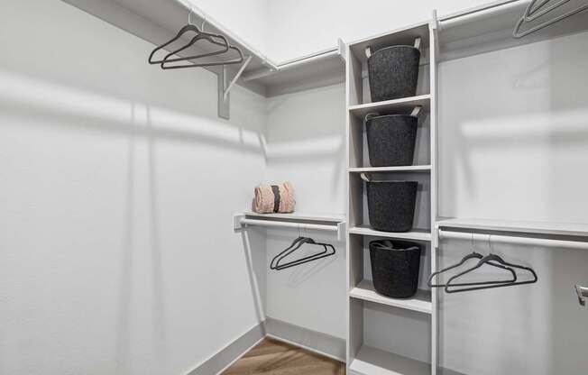 A white closet with clothes hanging and baskets on shelves.