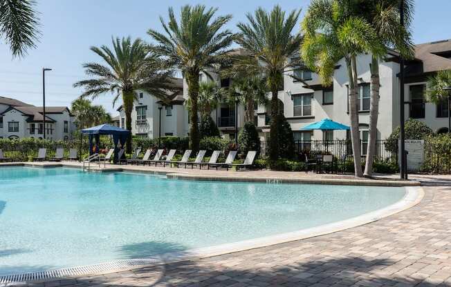 a large swimming pool with palm trees in front of an apartment building