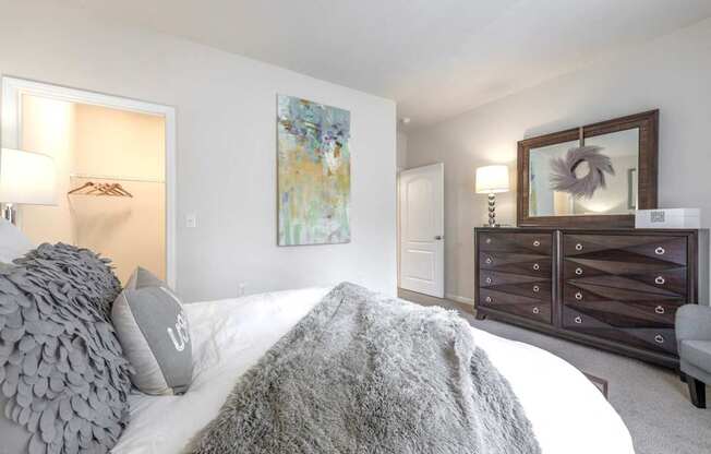 A bedroom with a white bed and a grey pillow.