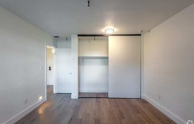 an empty living room with white walls and wood floors and a closet