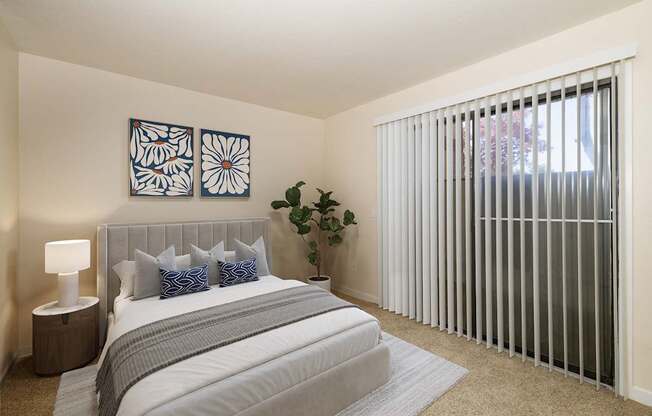 A bedroom with a bed, pillows, a lamp, and a plant.