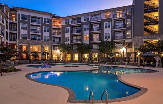 a swimming pool in front of an apartment building at night at The Tribute, Raleigh, NC, 27612
