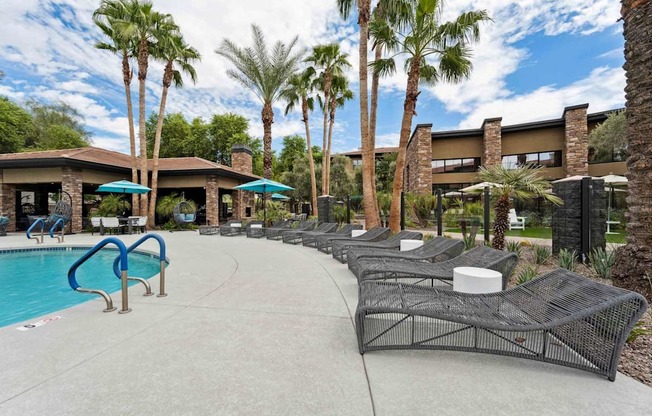 A pool area with a blue pool, lounge chairs, and palm trees. at The Laurel Apartments, Chandler, AZ