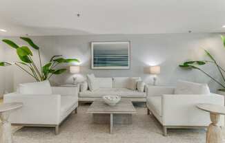 A modern living room with white furniture and a large painting on the wall.