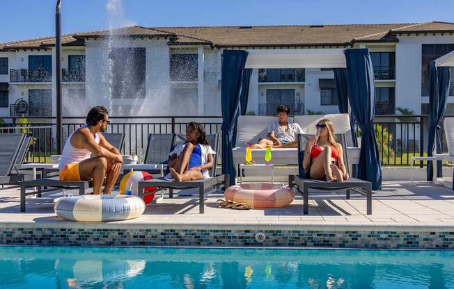 Four people are sitting by a pool with a waterfall in the background.