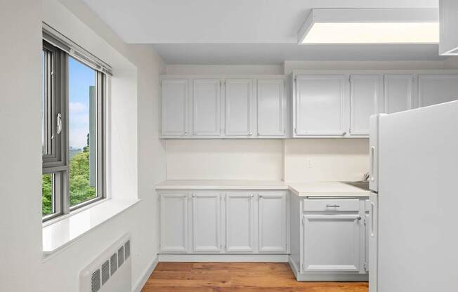 an empty kitchen with white cabinets and a window