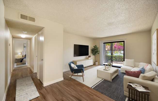 Living room with sectional couch, coffee table, tv on the wall and door to private patio