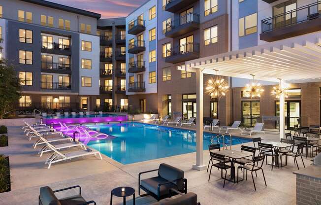 a pool area with lounge chairs and tables and a building in the background