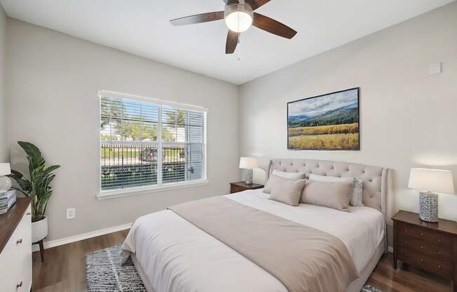 A bedroom with a large bed, a ceiling fan, and a painting on the wall.