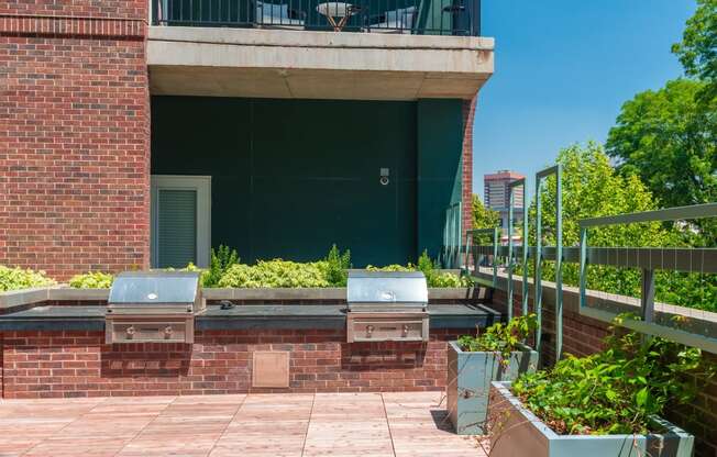 Red brick patio lounge with plants and two BBQ grills at Sylvan Uptown, Denver