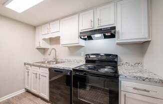 A black stove top oven sits in a kitchen with white cabinets.