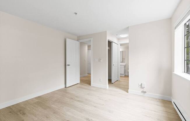 A room with white walls and wooden flooring with a doorway leading to another room.