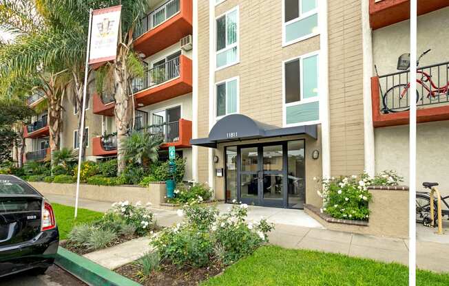 Mar Vista CA Apartments for Rent - Vista - Property Exterior with Tan Walls, White Trim, Orange Balconies, and Landscaped Plants Around the Front