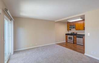 an empty living room and kitchen with wood cabinets and white carpet