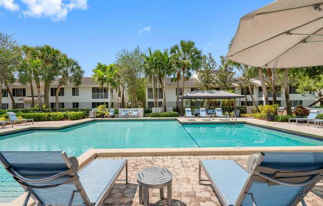 a swimming pool with chairs and umbrellas in front of an apartment building